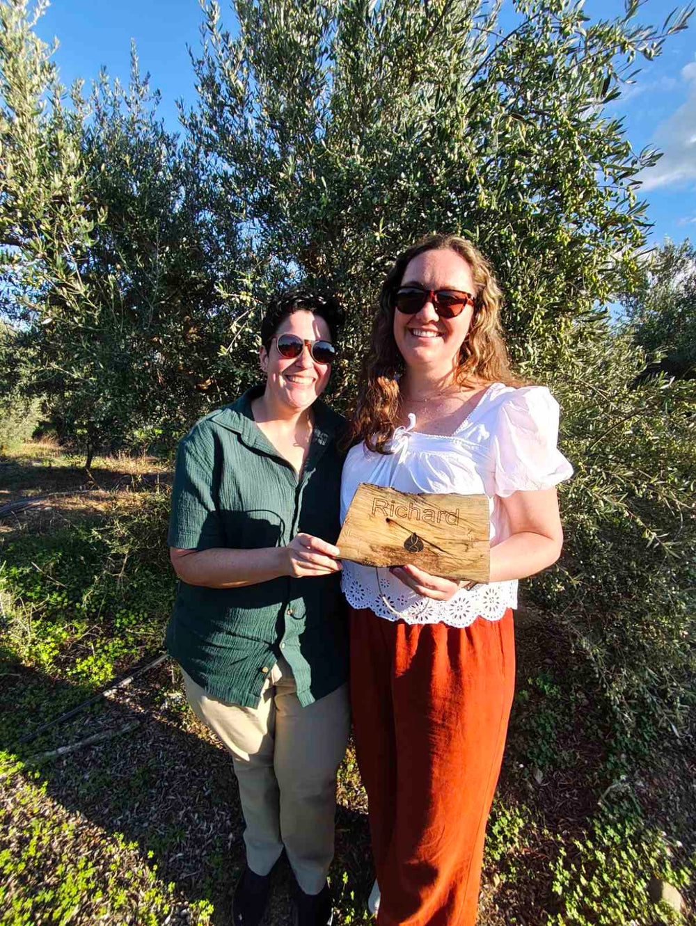 Two sisters from Florda,USA in front of the Olive Tree they adopted in Crete by Olivine holding their personalised wooden plaque with their name on it